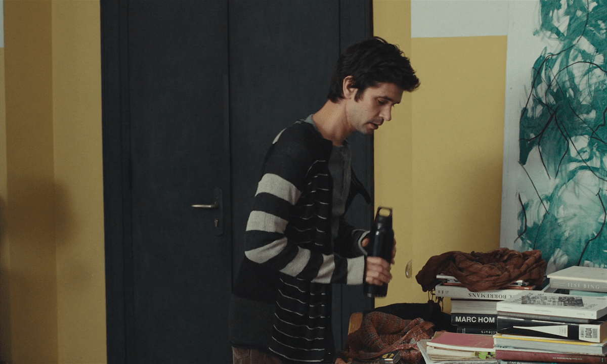 Clothes from Passages: Ben Whishaw looks down at some books while wearing a striped cardigan.