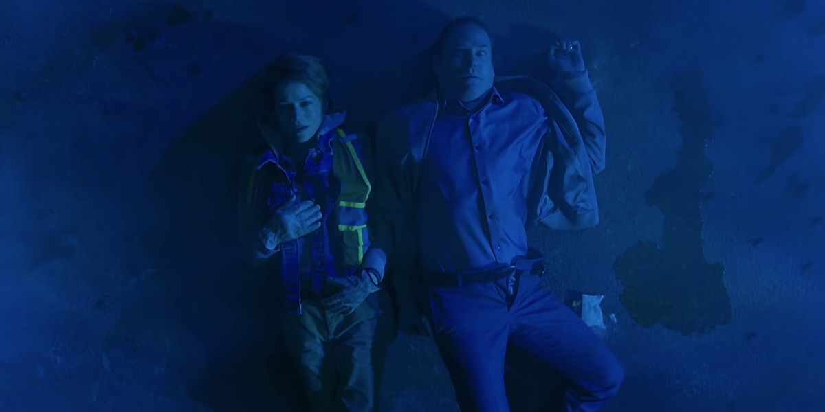 A blue light bathes a paralyzed Frederick Usher, Verna, dressed as a construction worker, lies beside him.
