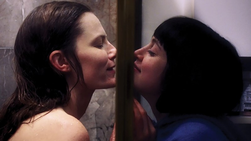 Queer horror to stream: The Carnivores. Lindsay Burge and Tallie Medel kiss through a shower door while smiling