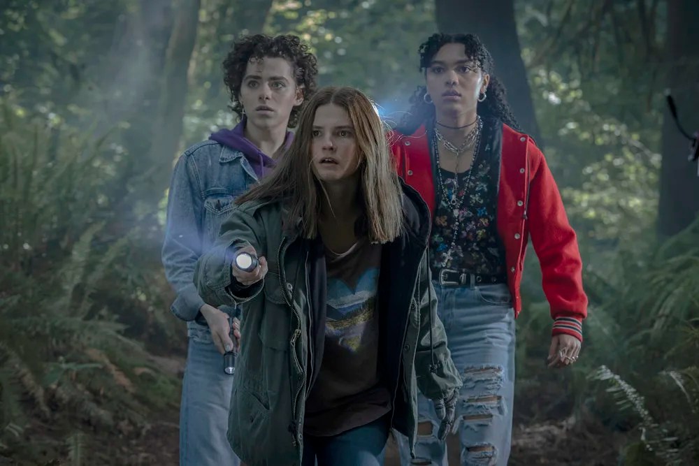 three teenagers in the woods with a flashlight, looking scared