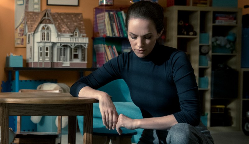 Theodora Crain in The Haunting of Hill House sits at a table with a doll house on it