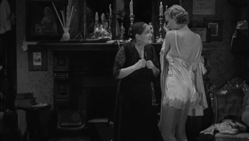 Queer horror to stream: The Old Dark House. A young woman in a neglige covers herself as an older woman looks on.
