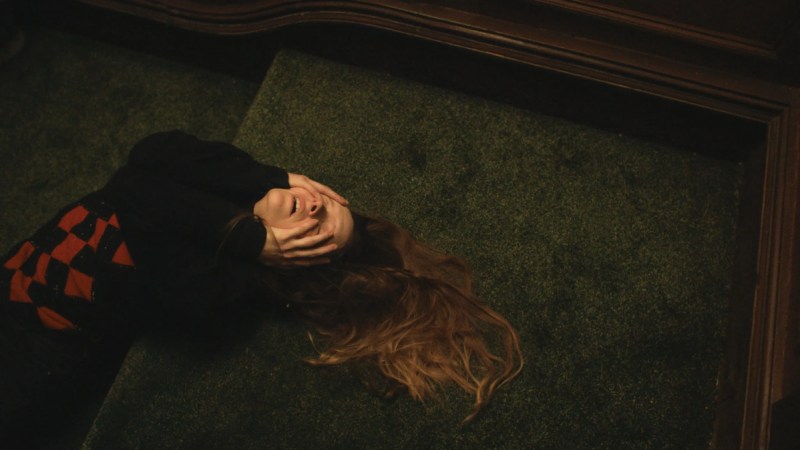 Queer horror to stream: Saint Maud. Shot from above, a woman with long red hair leans backward and clenches at her face.