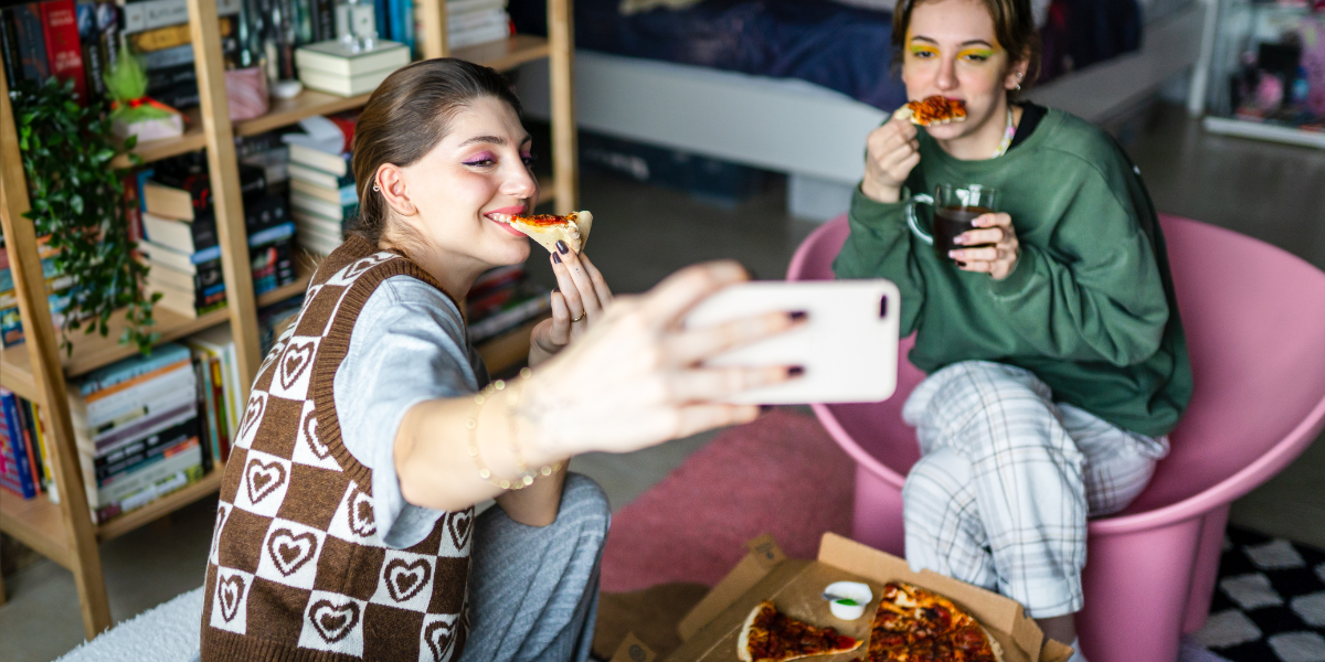 two young adults take a selfie while eating pizza