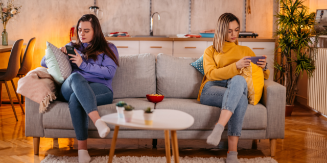 two women sit on the couch on their phones, not speaking or looking at each other