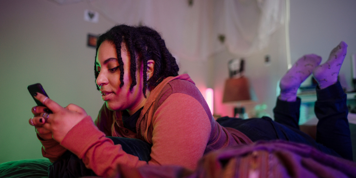 a queer person lays on their bed, scrolling on their phone