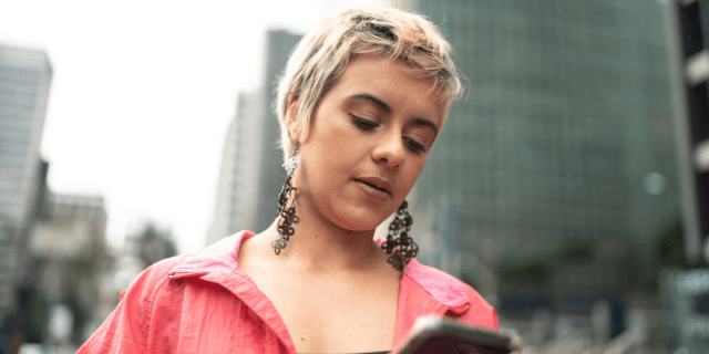 a woman with short bleached blond pixie style hair and dangly earrings is typing on a phone