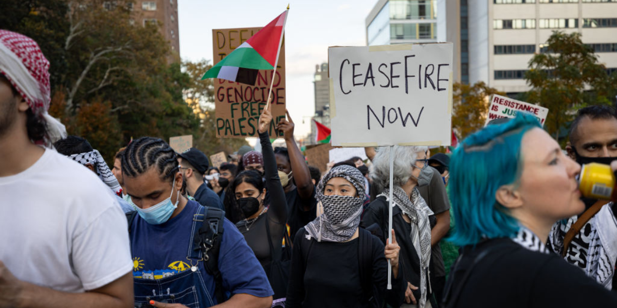 a group of protesters calling for a Ceasefire in Gaza line the streets of Brooklyn. one is holding a sign that says CEASEFIRE NOW