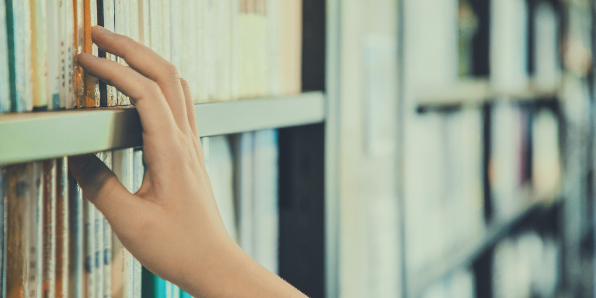 a hand reaches for books on a shelf