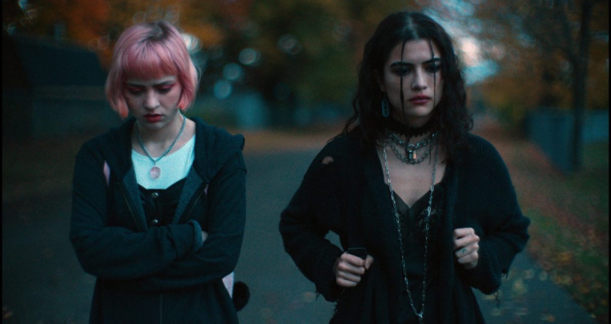 Queer horror to stream: We Need to Do Something. Sierra McCormick with pink hair and Lisette Alexis as goth walk on a fall day