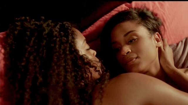 Sexy lesbian screenshot: Two women lie in bed. One is looking a the other's lips.