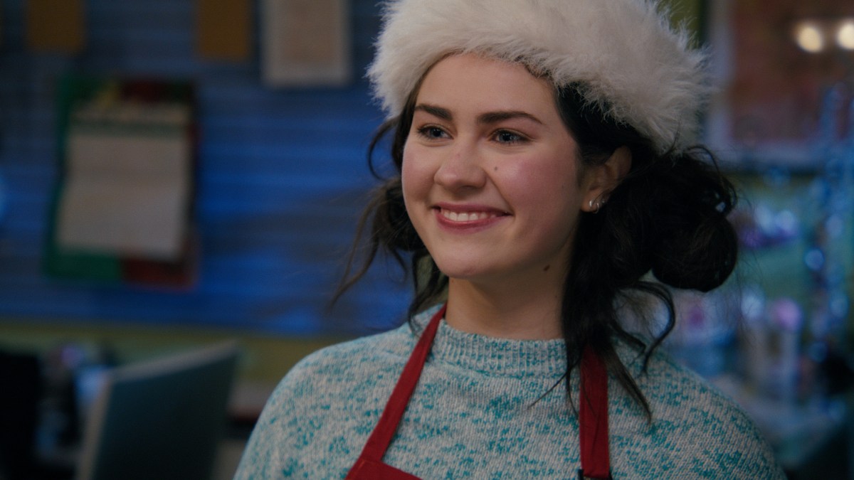 A teen girl in a Santa hat and and a blue and white sweater smiles.