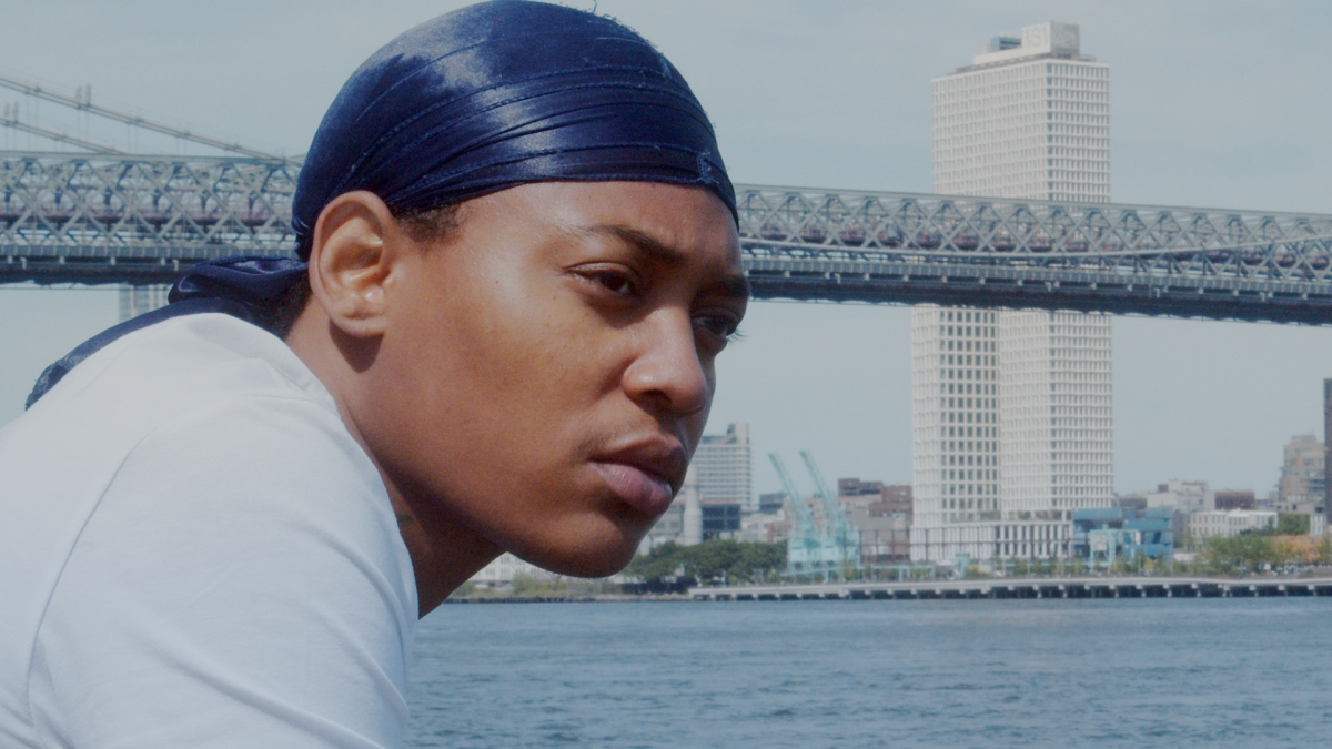 Beyond the Aggressives: A Black transmasc person looks out over the water with a city skyline behind them.