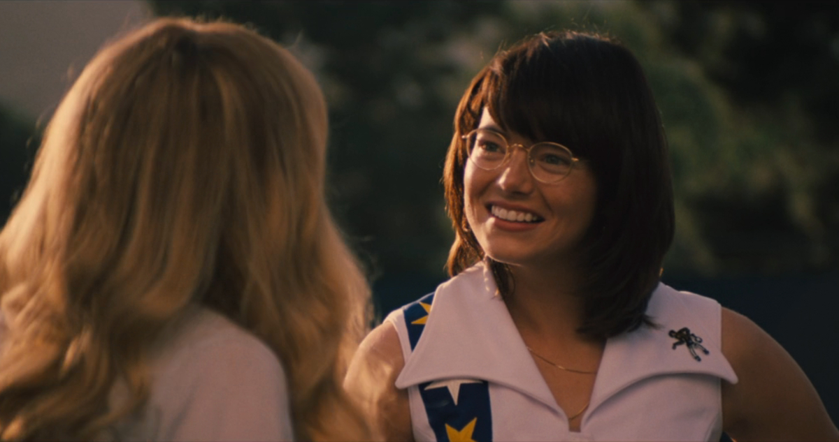 Emma Stone as Billie Jean King smiles at a woman while on a tennis court.