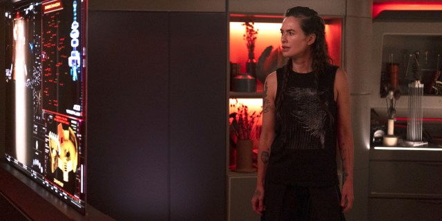 Beacon 23 screenshot of Lena Headey's character Aster standing in a black tank top with her tattoed arms showing. Her hair is in braids.