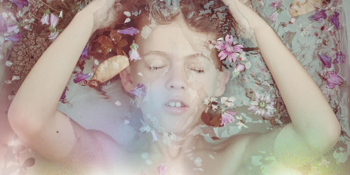 a young boy is submerged in water surrounded by flowers, light streams up from the bottom of the photo in a blur