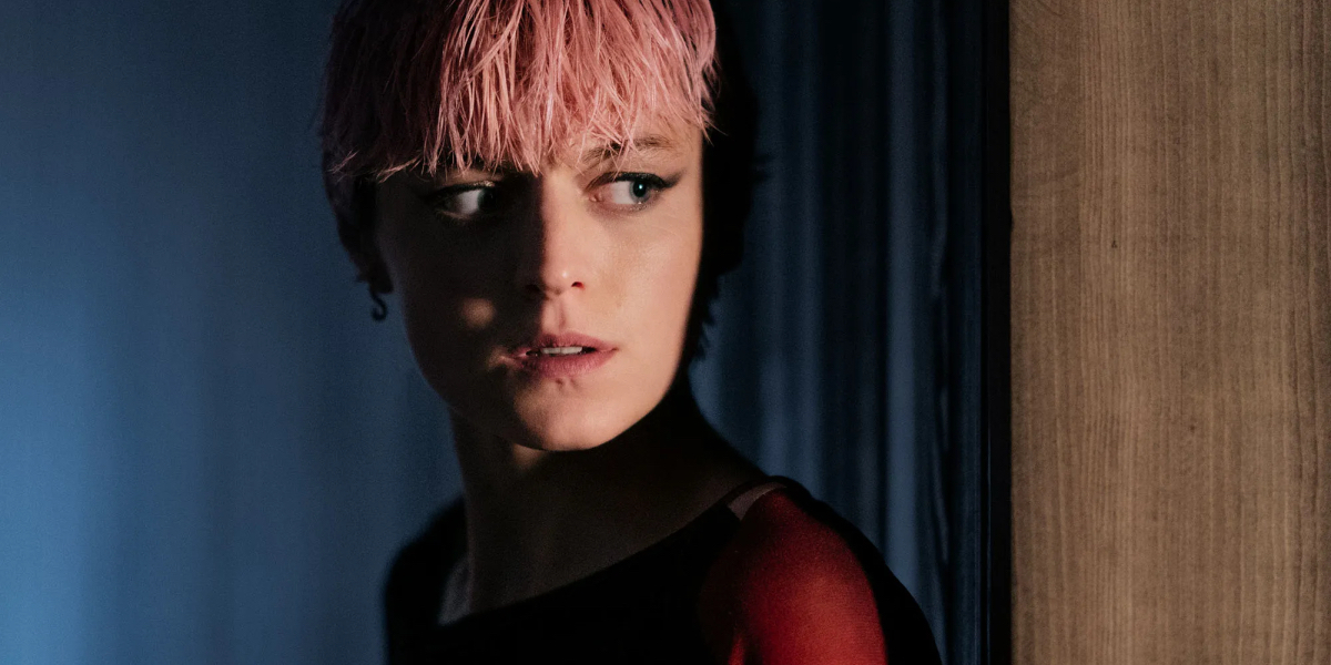 A Murder at the End of the World: A close up of Emma Corin with pink hair cloaked in shadows glancing to the side.