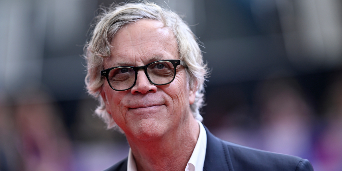 Close up of Todd Haynes in black rimmed glasses and an open collar black suit. He's smiling.