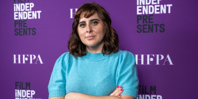 Maryam Keshavarz stands in front of a HFPA and Film Independent backdrop with her arms folded wearing a bright blue sweater.