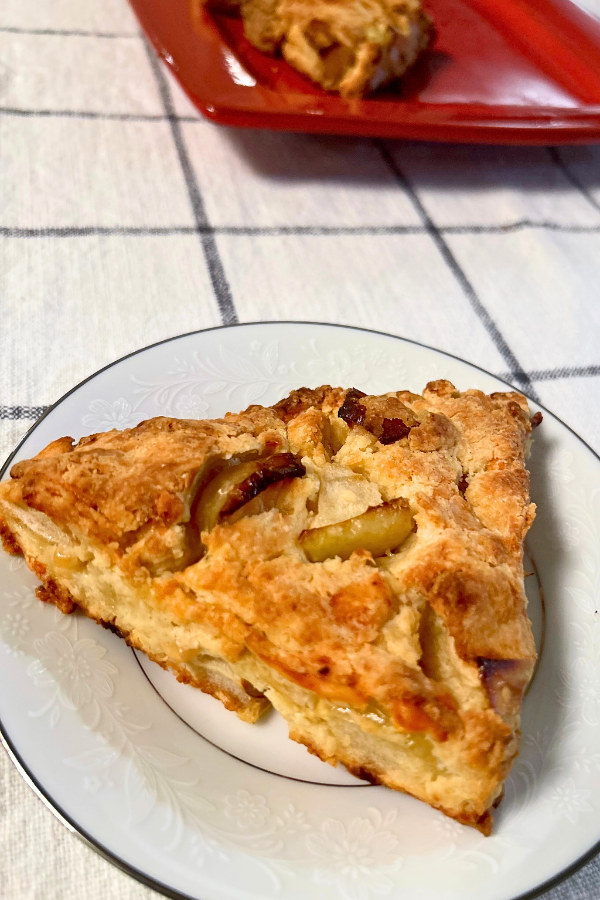 A close up of an apple cheddar scone on a white porcelain plate.