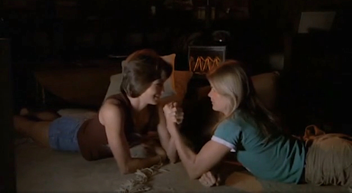 Two women arm wrestle while staring into each other's eyes.