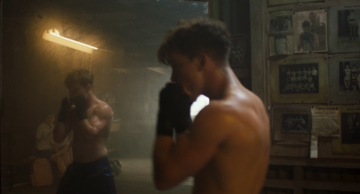 Queer sports movies: a teenage boy practices with a punching bag his reflection visible in the mirror beside him.