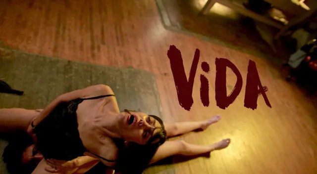 Mishel Prada leans back as she rides someone off camera. The title Vida appears in dark red next to her.
