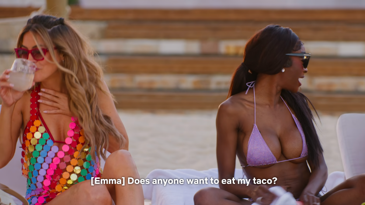 Real estate agents Chrishell Stause and Chelsea Lakhzani sit on a beach in Cabo San Lucas while real estate Emma Hernan (off-screen) asks the group “Does anyone want to eat my taco?”