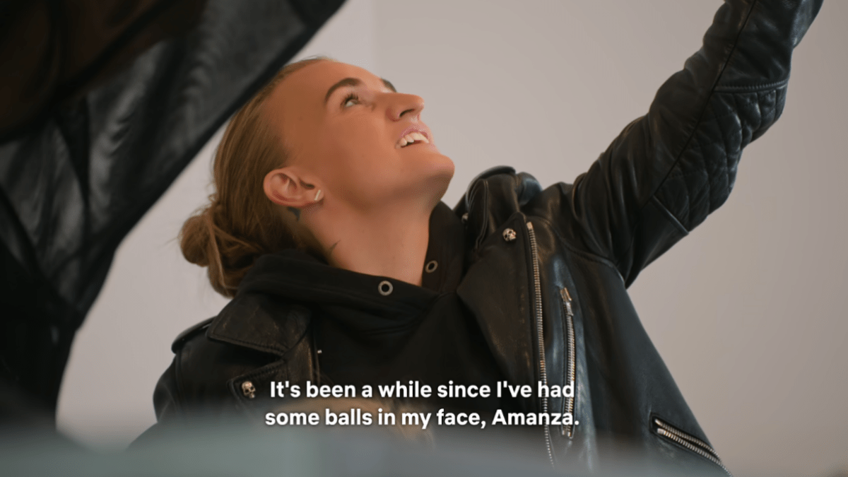 Non-binary musician G Flip reaches up towards a lighting fixture while saying “It’s been a while since I’ve had some balls in my face, Amanza.”
