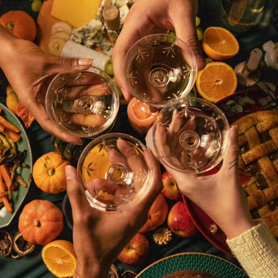 four hands toasting drinks over a sumptuous fall spread