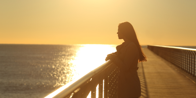 a woman on a boardwalk looking out at the sea on a sunny day