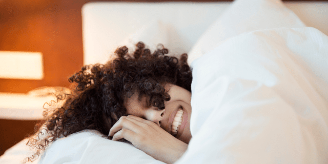 a woman with curly hair laying in bed smiling