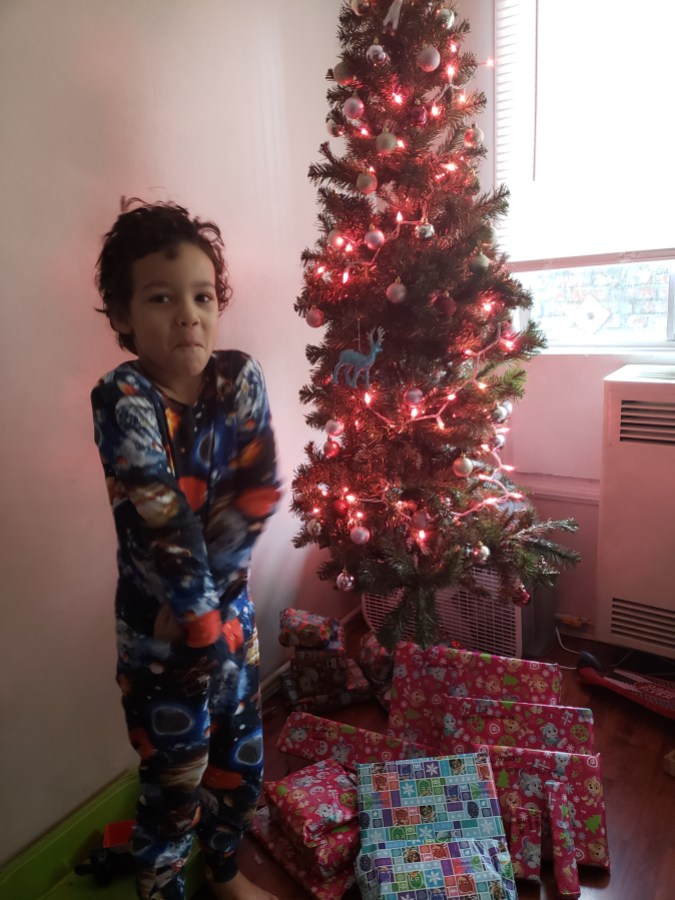 the author's young son standing in front of a christmas tree with presents under it