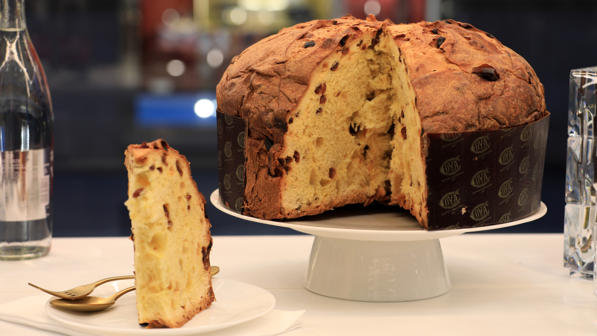 A full panettone on display next to a slice from the panettone on a plate.