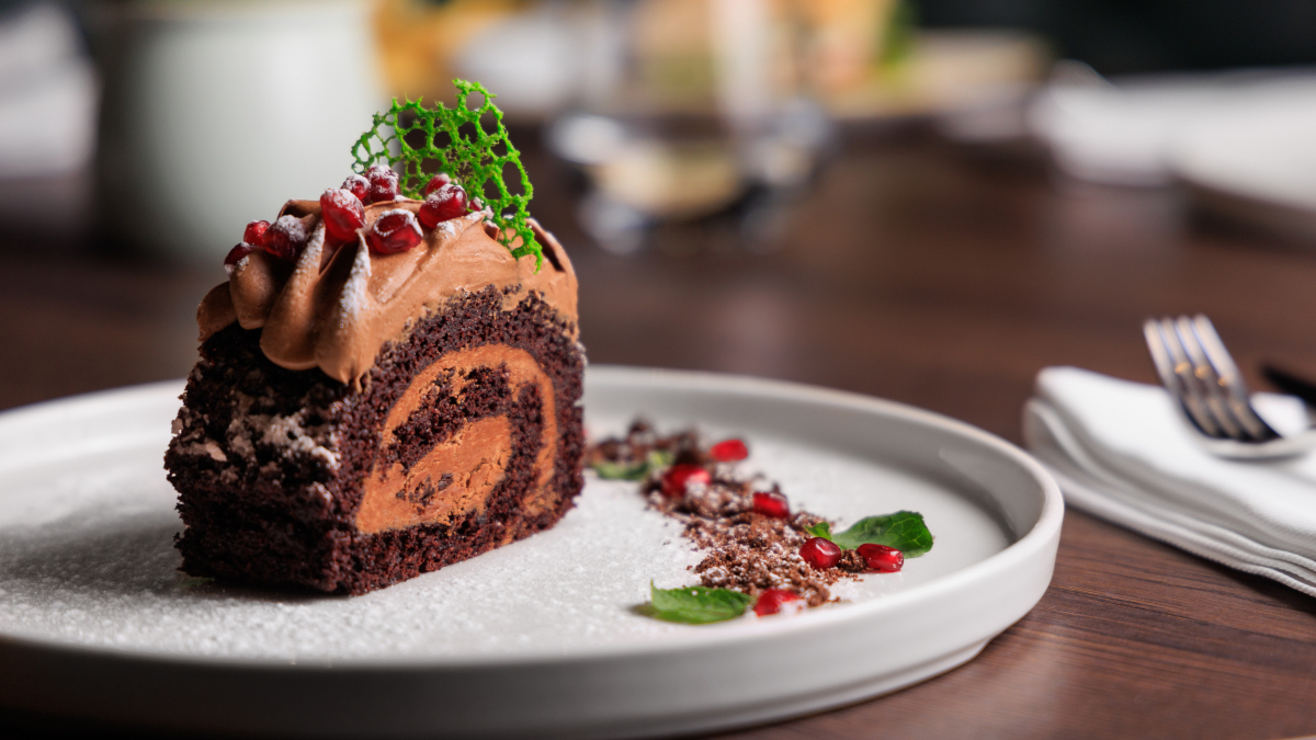 Italian Christmas Desserts: a fancy slice of Italian yule log cake beautifully plated with pomegranate seeds and a green garnish