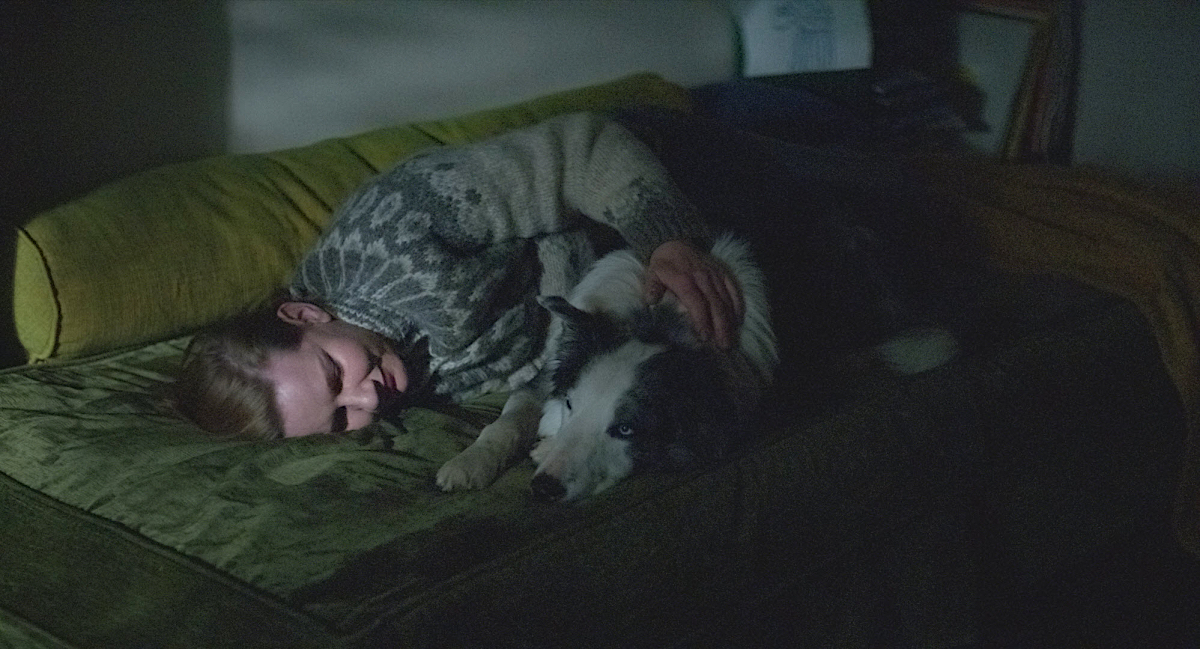 Sandra Hüller lies in a couch cuddling with her dog in the dark.