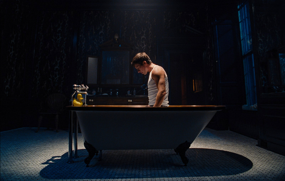 Best queer movie scenes of 2023: In a dark bathroom Barry Keoghan sits on his knees in a bathtub and stairs at the emptying drain.