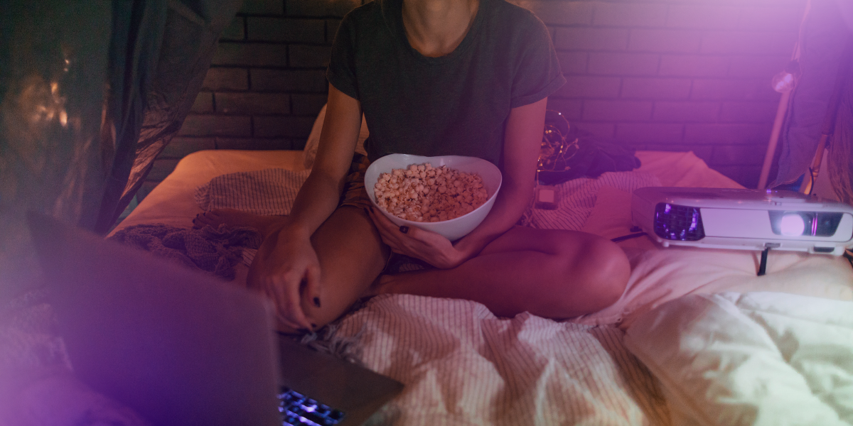 a woman with a bowl of popcorn about to watch a movie in bed