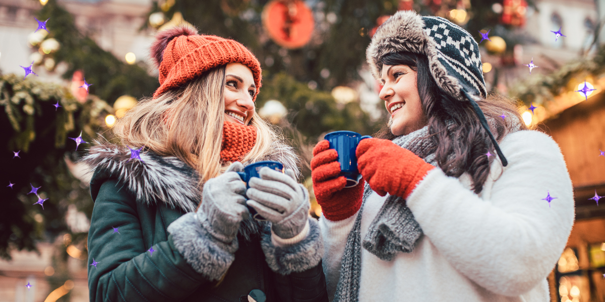 two women at a holiday market on a date having hot cocoa