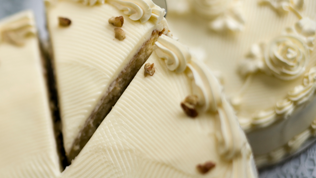 A close up of an Italian cream cake with a slice cut and being removed