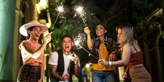 A group of queer-looking friends light sparklers with big smiles.