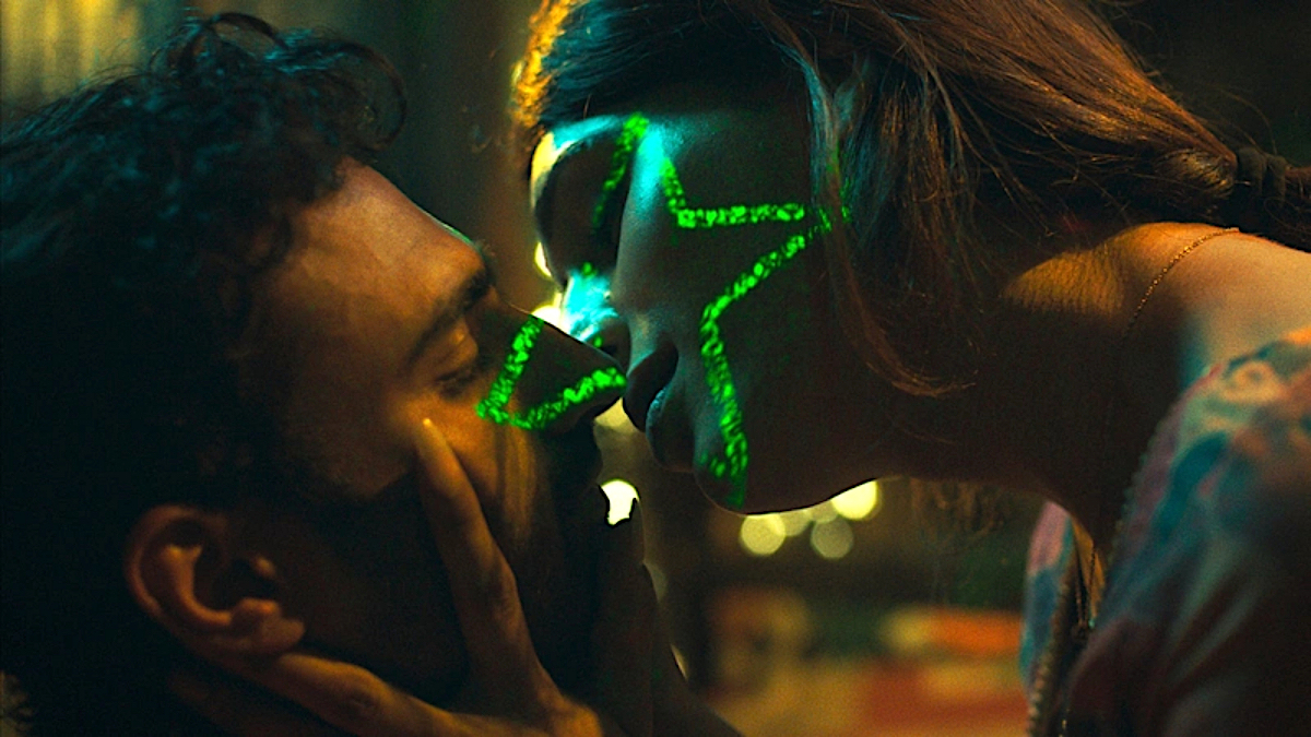 A trans woman bends down to kiss a cis man as their faces are lit up by the pattern of a green star.