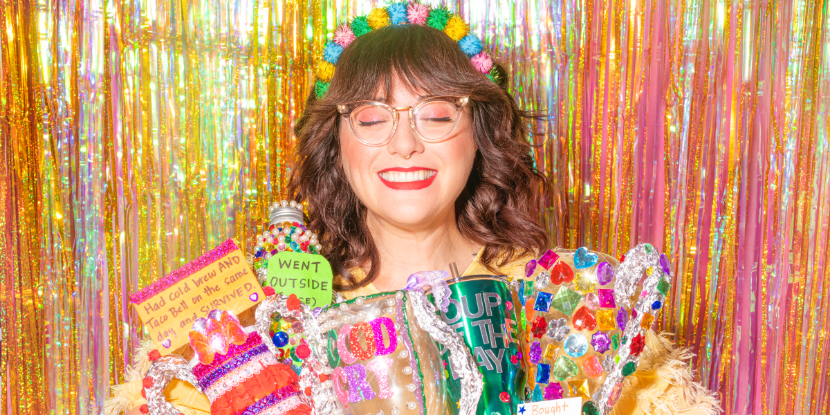 Shitty Craft Club: Sam Reece smiles with her eyes closed, sparkly streamers behind her, and home made awards in her hands.