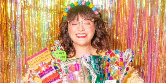 Shitty Craft Club: Sam Reece smiles with her eyes closed, sparkly streamers behind her, and home made awards in her hands.