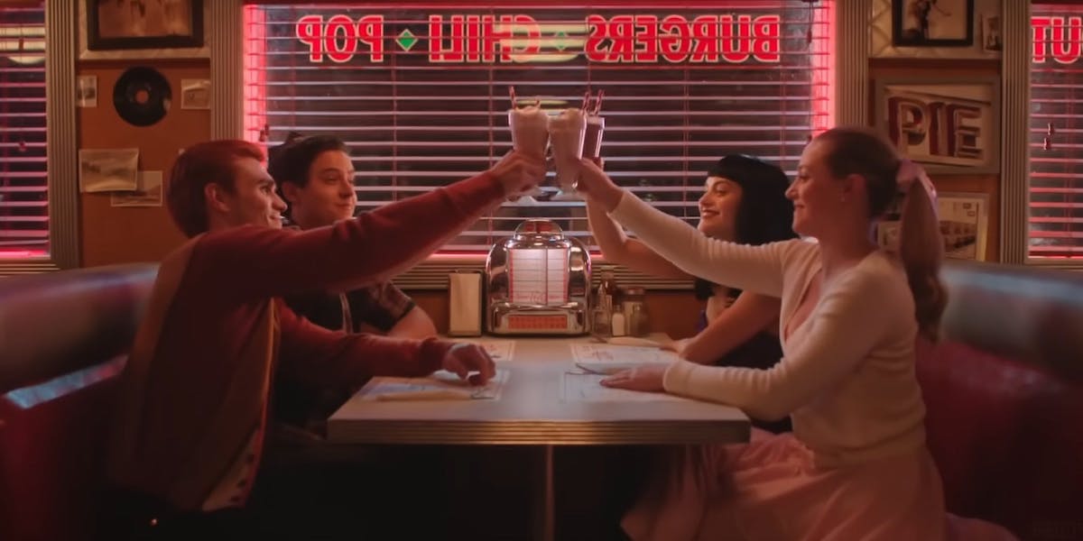 The four main characters of Riverdale cheers milkshakes in the booth of a diner.
