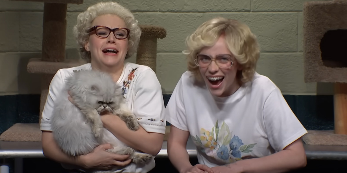 Kate McKinnon and Billie Eilish holding a cat and laughing in the Whiskers R We sketch.