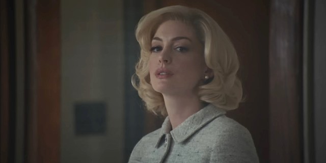 Eileen: Anne Hathaway in a blonde wig purses her lips and looks toward the camera.