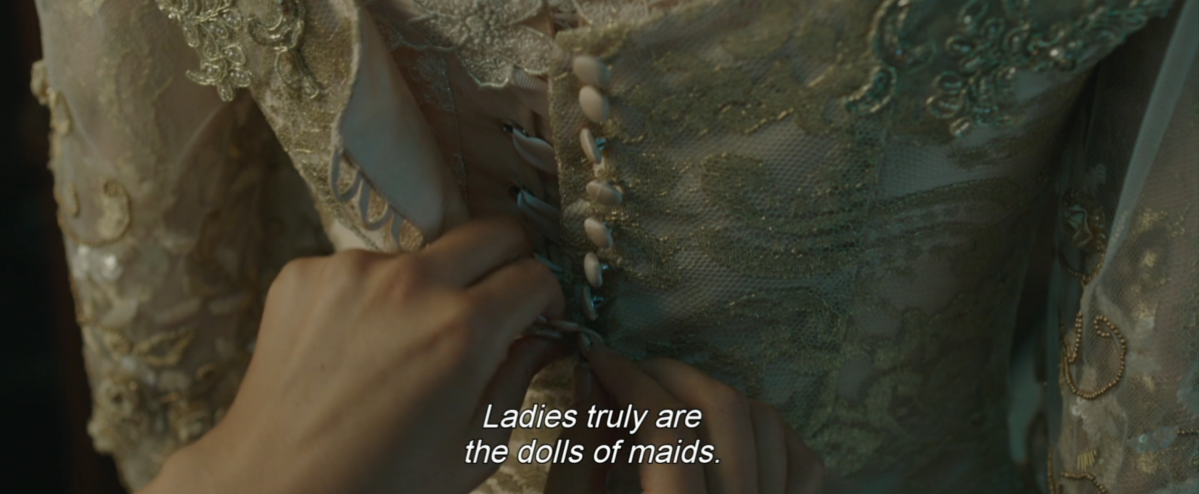 a close up of hands buttoning a dress, with the narration Ladies truly are the dolls of maids