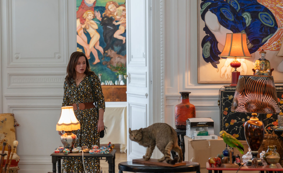 Laura Calamy walks into a room in a mansion, a taxidermied cat is center frame.