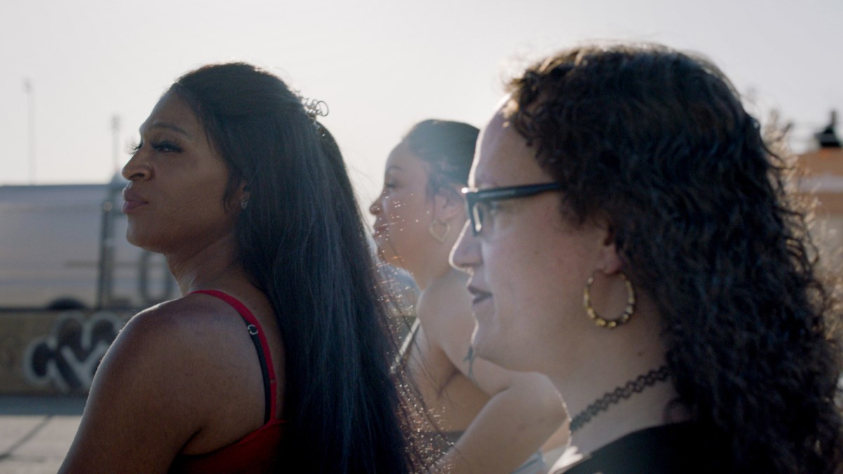 Three trans women — including Kristen Lovell — look out over a pier. 